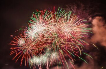 Colorful fireworks illuminating the night sky above a serene water body, creating a festive atmosphere.