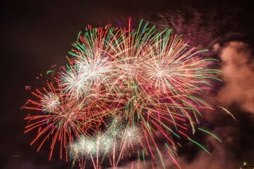 Colorful fireworks illuminating the night sky above a serene water body, creating a festive atmosphere.